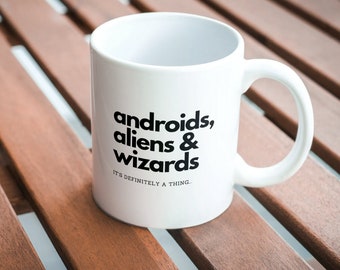 May include: White ceramic mug with black text that reads "androids, aliens & wizards it's definitely a thing."