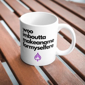 May include: White ceramic mug with black text that reads "woo imboutta makeaname formyslfere" and a purple spade symbol.
