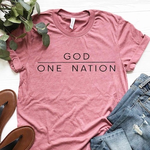 May include: A heather pink t-shirt with the text "GOD ONE NATION" printed in black.