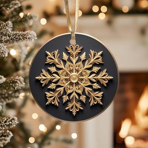 May include: A round Christmas ornament with a gold snowflake design on a black background. The snowflake is intricately detailed with a three-dimensional effect. A gold ribbon is attached for hanging. The ornament is approximately 4 inches in diameter.