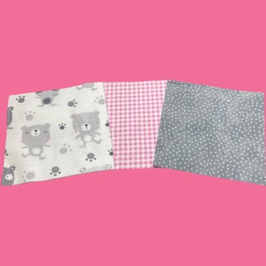 May include: Three fabric squares on a pink background. One square features a pattern of gray bears and paw prints on a white background. Another is pink gingham. The third is gray with white polka dots.