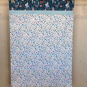 May include: A white fabric kitchen towel with a repeating pattern of nutcracker soldiers, musical instruments, and other holiday-themed imagery. The top of the towel features a dark blue fabric with a repeating pattern of nutcracker soldiers, snowflakes, and holly.