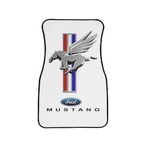 Könnte beinhalten: Weiße Autofußmatte mit einem silbernen Ford Mustang-Logo, das ein galoppierendes Pferd mit Flügeln zeigt. Das Logo ist von roten, weißen und blauen Streifen umgeben. Der Text "Ford Mustang" ist unter dem Logo gedruckt.