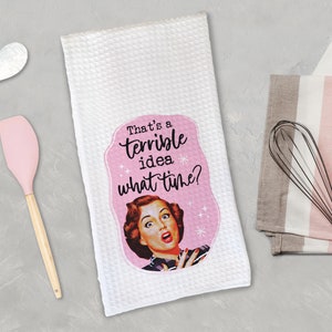 May include: White kitchen towel with a pink border and a retro-style illustration of a woman with the text "That's a terrible idea. What time?"