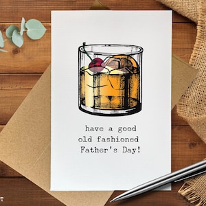 May include: Father's Day greeting card featuring a detailed illustration of an Old Fashioned cocktail with ice, a cherry, and an orange slice. The card reads "have a good old fashioned Father's Day!" on a white background.