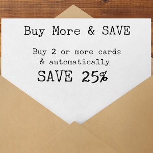 May include: A white card inside a brown envelope with the text "Buy More & SAVE". The card states "Buy 2 or more cards & automatically SAVE 25%" in a typewriter-style font. The background is a wooden surface.