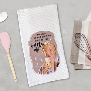 May include: White kitchen towel featuring a vintage-style illustration of a woman holding a glass of bubbly. The text reads "because it's not good to keep things bottled up".