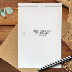 May include: A white greeting card, 4 inches wide and 6 inches tall, with the text "BLANK INSIDE FOR YOUR PERSONAL MESSAGE". The card is on a brown envelope, with a silver pen resting on the surface. The background is a wooden table.