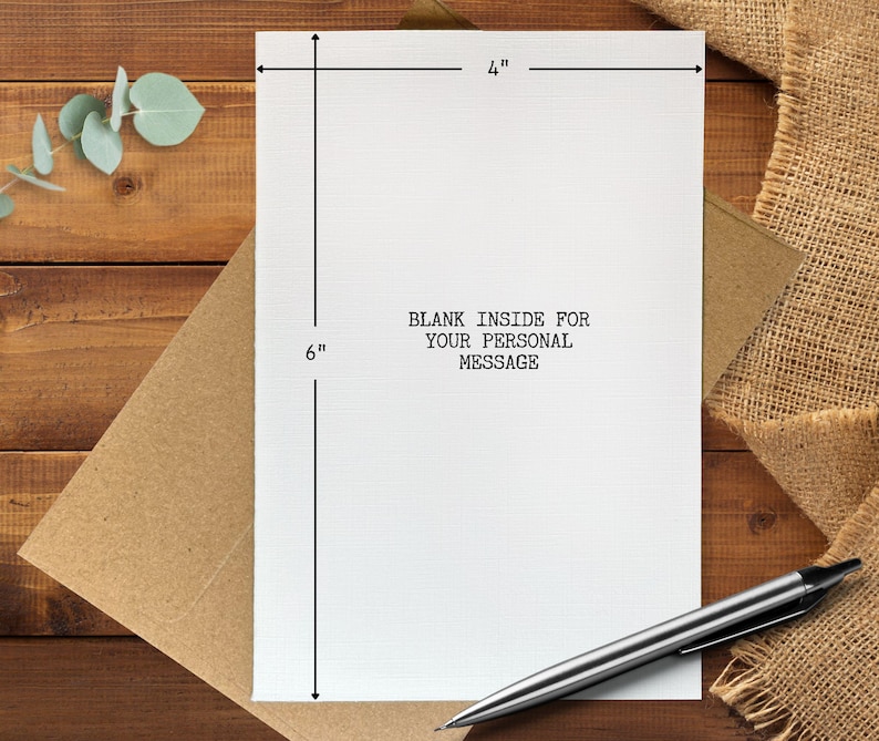 May include: A white greeting card, 4 inches wide and 6 inches tall, with the text "BLANK INSIDE FOR YOUR PERSONAL MESSAGE". The card is on a brown envelope, with a silver pen resting on the surface. The background is a wooden table.