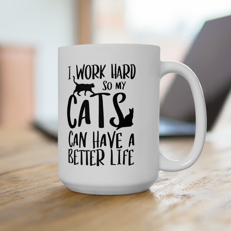 May include: White ceramic coffee mug with black text that reads "I work hard so my cats can have a better life". The mug has a black silhouette of two cats on it.
