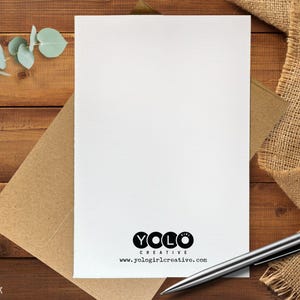 May include: A blank white card with a brown envelope, a silver pen, and a burlap cloth on a wooden surface. The card has the text "YOLO CREATIVE" and the website address "www.yologirlcreative.com".