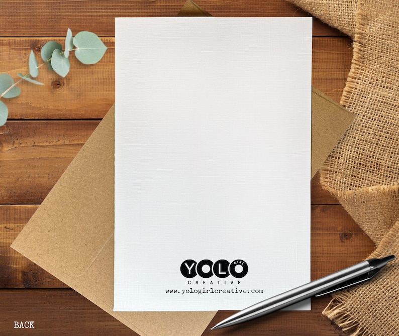 May include: A blank white card with a brown envelope, a silver pen, and a burlap cloth on a wooden surface. The card has the text "YOLO CREATIVE" and the website address "www.yologirlcreative.com".