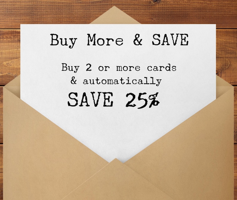 May include: A white card inside a tan envelope with the text "Buy More & SAVE". The card also states "Buy 2 or more cards & automatically SAVE 25%" in a typewriter-style font. The background is a wooden surface.