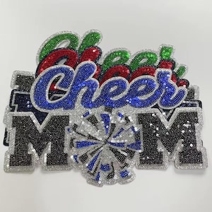 May include: A decorative applique with the words "Cheer Mom" in blue, red, and green sequins. The letters "MOM" are in black sequins with a silver glitter border. A silver and blue sequin pom-pom is in the center.