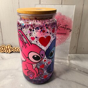 Puede incluir: Un vaso de vidrio transparente con tapa de madera, con un dise&ntilde;o de personajes de dibujos animados rosas y azules con corazones. El vaso est&aacute; lleno de purpurina y confeti peque&ntilde;o en forma de coraz&oacute;n. Una bolsa transparente con la palabra "Kreations" est&aacute; en el fondo.