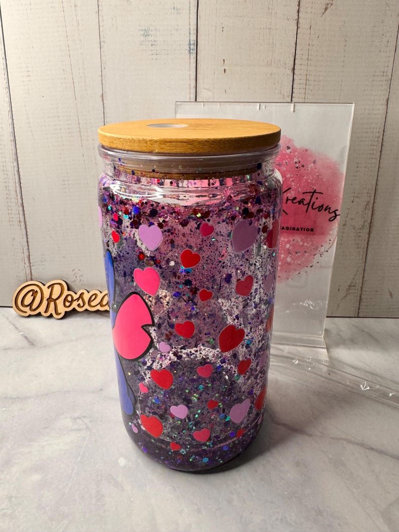 Puede incluir: Un tarro de vidrio transparente con tapa de madera, lleno de purpurina morada, confeti en forma de coraz&oacute;n y un dise&ntilde;o de personaje de dibujos animados. El tarro es de estilo vaso, adecuado para bebidas fr&iacute;as.