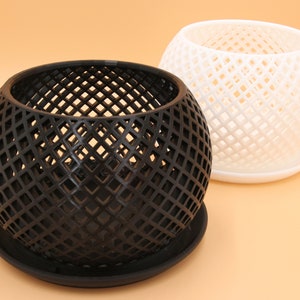 May include: Two round, geometric planters with a diamond pattern. One planter is black and the other is white. Both planters have a matching saucer.