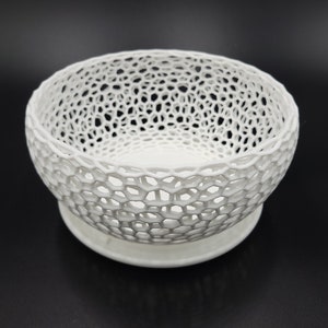 May include: A white ceramic bowl with a delicate, intricate lattice design. The bowl has a wide, round base and a slightly flared rim.