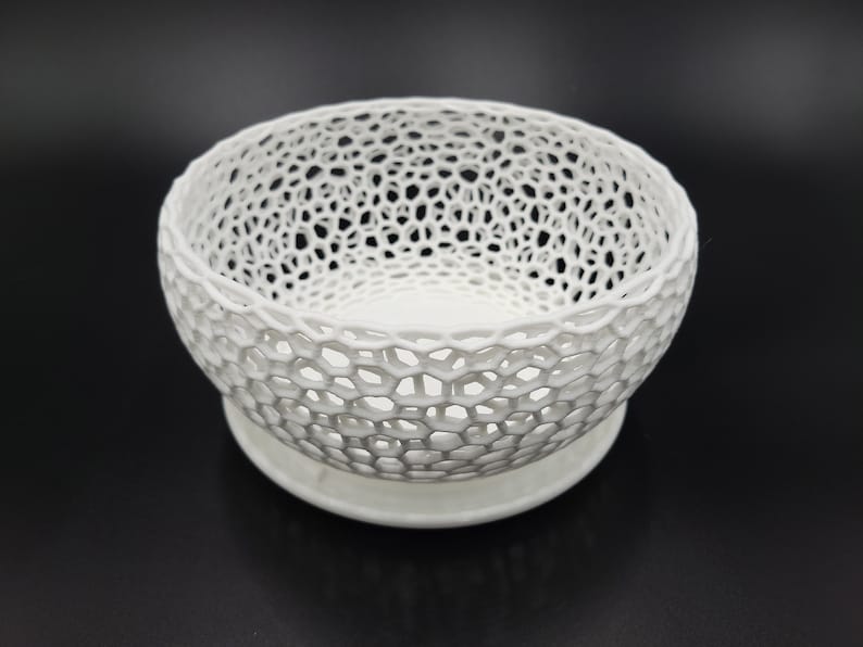 May include: A white ceramic bowl with a delicate, intricate lattice design. The bowl has a wide, round base and a slightly flared rim.