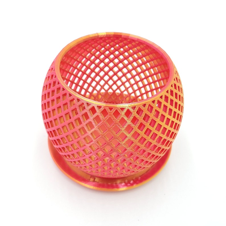 May include: A pink and gold geometric planter with a round, open-weave design. The planter has a small base.