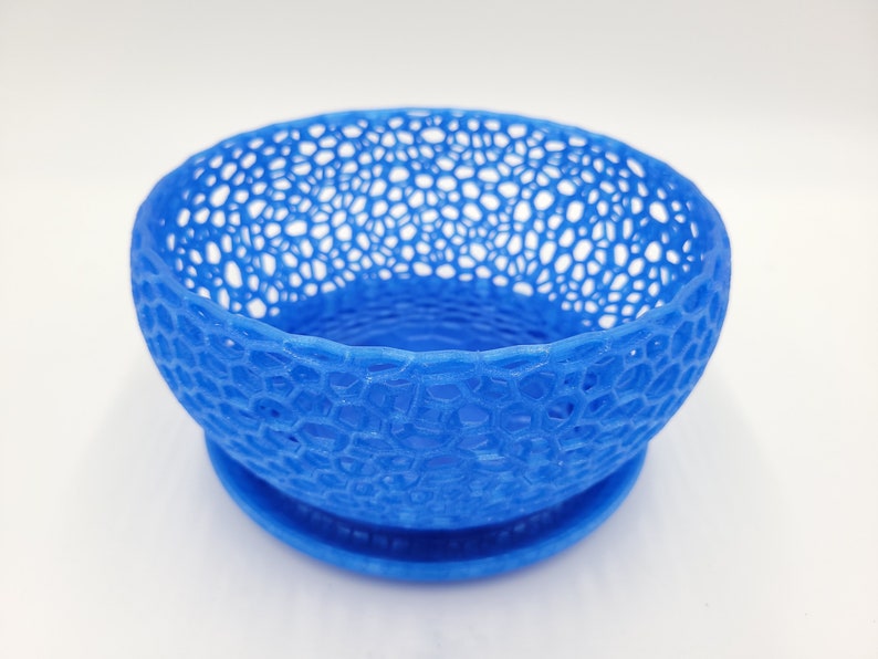 May include: A blue, 3D printed bowl with a lacy, openwork design. The bowl has a matching base.