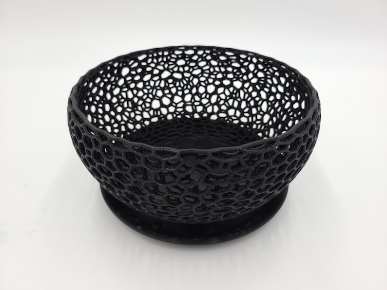 May include: A black, 3D printed bowl with a geometric, honeycomb-like design. The bowl has a solid base and is perfect for holding small items.
