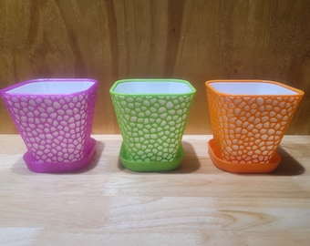 May include: Three plastic flower pots with a textured design. The pots are purple, green, and orange.