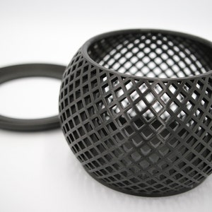 May include: A black metal candle holder with a geometric design. The holder is shaped like a sphere with a circular opening at the top. The holder is made of a wire mesh.