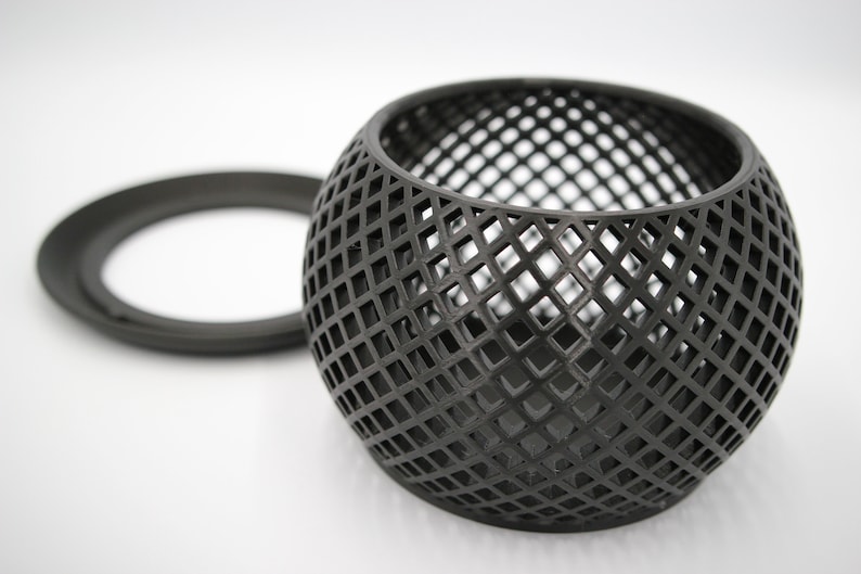May include: A black metal candle holder with a geometric design. The holder is shaped like a sphere with a circular opening at the top. The holder is made of a wire mesh.