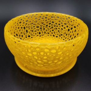 May include: A yellow, 3D printed bowl with a lacy, openwork design. The bowl is round and has a wide, shallow base.