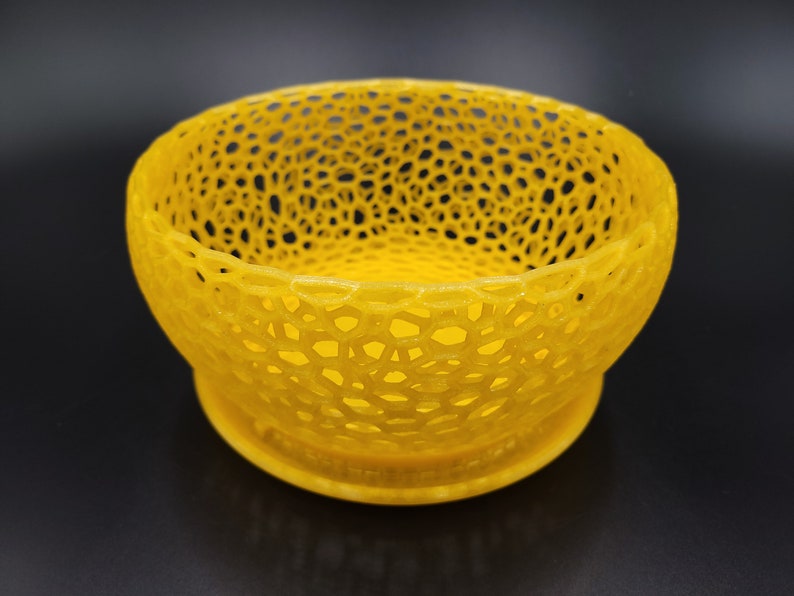 May include: A yellow, 3D printed bowl with a lacy, openwork design. The bowl is round and has a wide, shallow base.