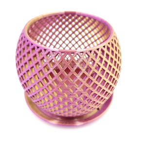 May include: A pink and gold metal planter with a geometric design. The planter is round and has a base.