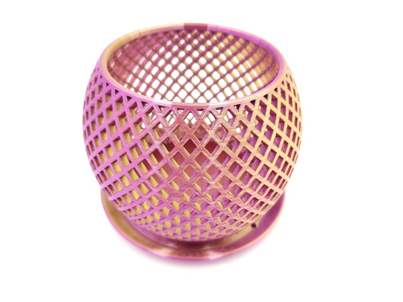 May include: A pink and gold metal planter with a geometric design. The planter is round and has a base.
