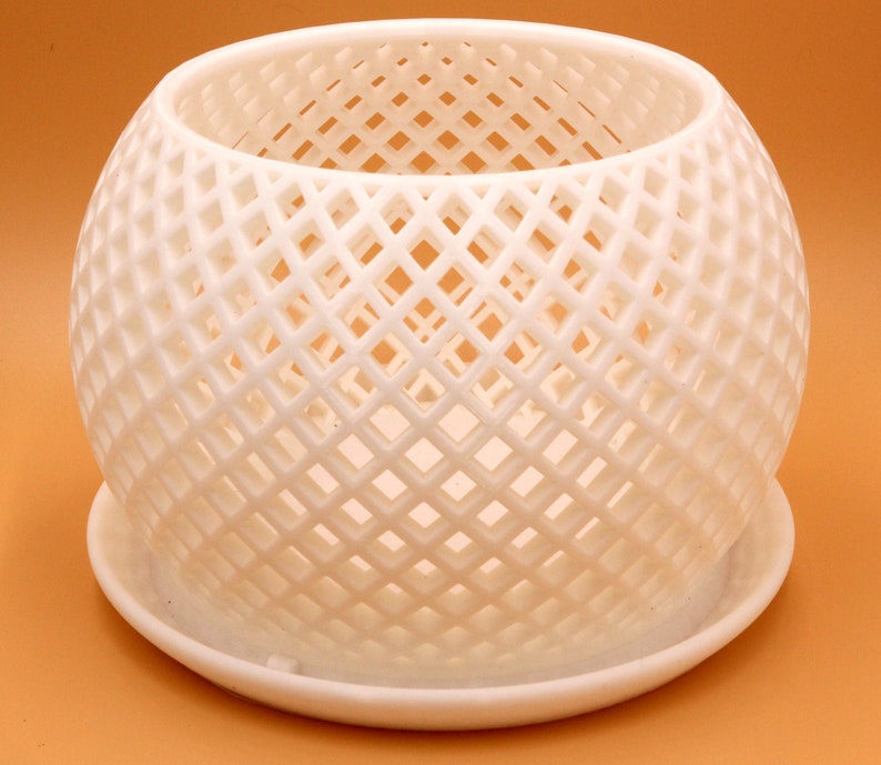 May include: White ceramic planter with a geometric, diamond-shaped lattice design. The planter has a separate saucer.