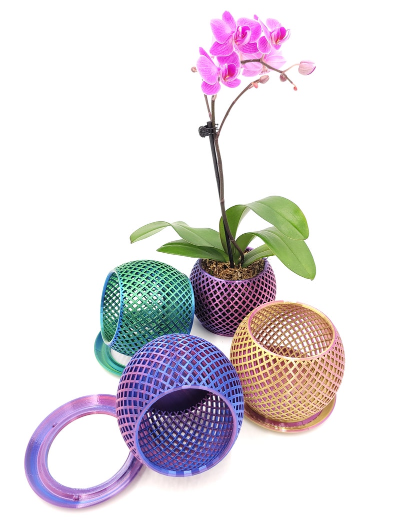 May include: Four iridescent, geometric, spherical planters with a pink orchid plant in one of the planters. The planters are made of a mesh-like material and have a metallic finish.