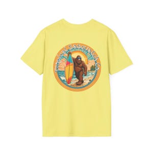 May include: Yellow short-sleeved t-shirt with a circular graphic of a Bigfoot holding a surfboard. The graphic has the text "Tropical Sasquatch Co." and "Maui, Hawaii" in a retro font.