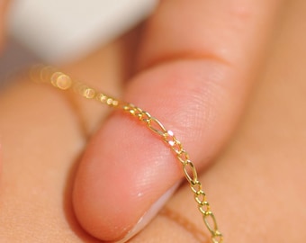 May include: A delicate gold chain bracelet with a repeating pattern of small links. The bracelet is being held by a person's fingers, showcasing its fine details and the warm tone of the gold. The jewelry is a simple yet elegant accessory.