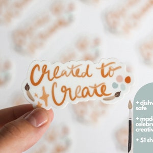 May include: A white sticker with the text "Created to Create" in orange script. The sticker has a paintbrush, stars, and paint splatters in orange, brown, and blue.