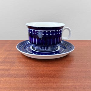 Może przedstawiać: Niebiesko-biały zestaw filiżanki i spodka ceramicznego. Filiżanka ma ciemnoniebieski wzór z kółek i linii pionowych. Spodek ma pasujący wzór. Filiżanka ma białe wnętrze i mały uchwyt.