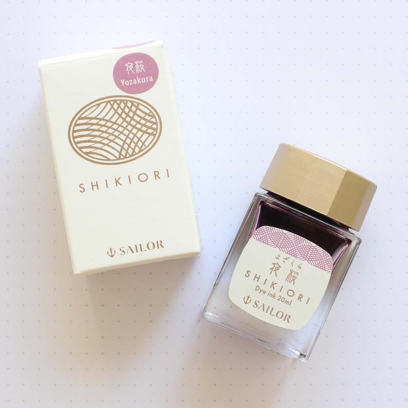 A clear glass bottle of Shikiori dye ink, 20ml, with a gold cap and a label featuring Japanese text and a pink design. Beside it is a white box with the Shikiori logo and text, and the Sailor logo.