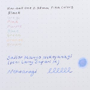 A close-up of a white paper with handwritten ink swatches in various colors. The text includes "Uni-ball One 0.38mm Fika Colors" and "Sailor Manyo Nekoyanagi". Colors include black, grey, pink, purple, blue, green, orange, and brown.