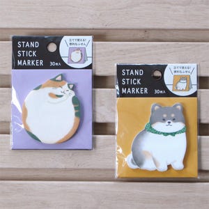 May include: Two packs of stand stick markers. One shows a cartoon cat in orange, white, and green, the other a dog in grey, white, and green. Each pack has the text "STAND STICK MARKER 30枚入".