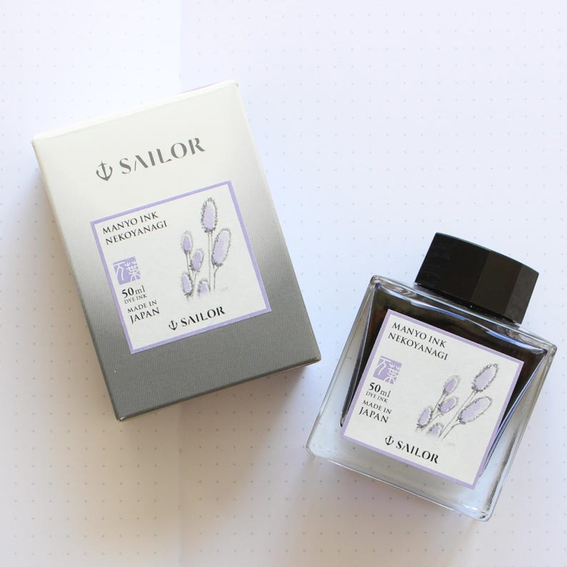 A clear glass ink bottle and matching box. The bottle and box have labels with the text "MANYO INK NEKOYANAGI" and "SAILOR". The labels also feature a floral illustration and state the ink volume is 50ml. The box is gray and white.