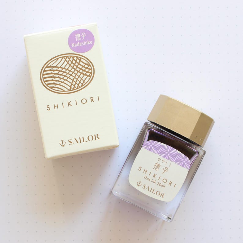 A clear glass bottle of Shikiori dye ink, 20ml, with a gold cap and a white label with Japanese text. The ink is a light purple color. A matching box with the text "SHIKIORI" and "SAILOR" is next to the bottle.