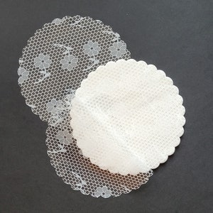 May include: Two white lace doilies, one on top of the other, with a scalloped edge. The top doily is slightly smaller than the bottom doily.
