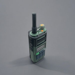 May include: A green and black two-way radio with a black antenna and a small orange button. The radio has a small screen and several buttons.