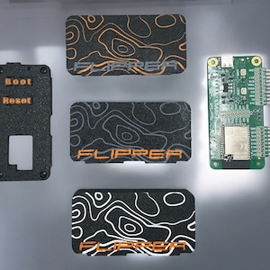 May include: A green circuit board with a black and white patterned case, a black case with the words "Boot" and "Reset" printed in orange, and three black and white patterned cases with the word "Flipper" printed in orange.