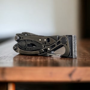 May include: A black multi-tool with a variety of tools, including pliers, a knife, and a saw. The tool is closed and has a black handle.