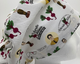 Puede incluir: Un gorro de quirófano blanco con un patrón repetido de remolachas, las palabras "Schrute Farms" y un retrato de Dwight Schrute de la serie de televisión "The Office". El texto "Schrute Farms" se repite con las palabras "People Love Beets" y "Bed & Breakfast".