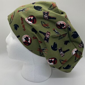May include: Green fabric scrub hat with a repeating pattern of Freddy Krueger's face, a claw, and a sign that says "Elm St. Springwood" in black and white text.
